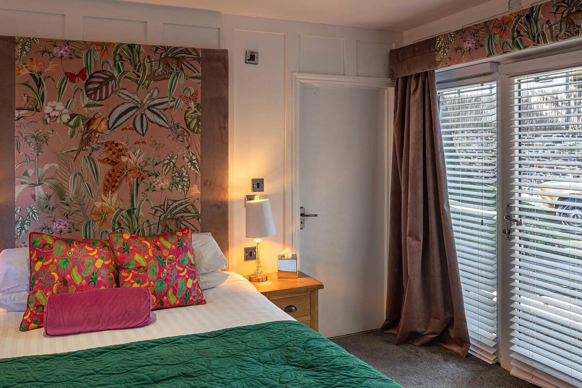 A hotel room with a bed, a nightstand, a lamp, and a window with curtains.