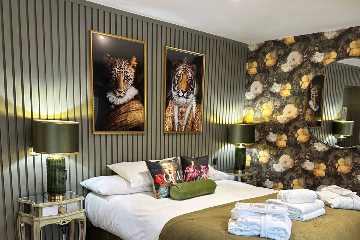 A bedroom with a large bed, two wall-mounted lamps, a mirror, and a floral wallpaper.
