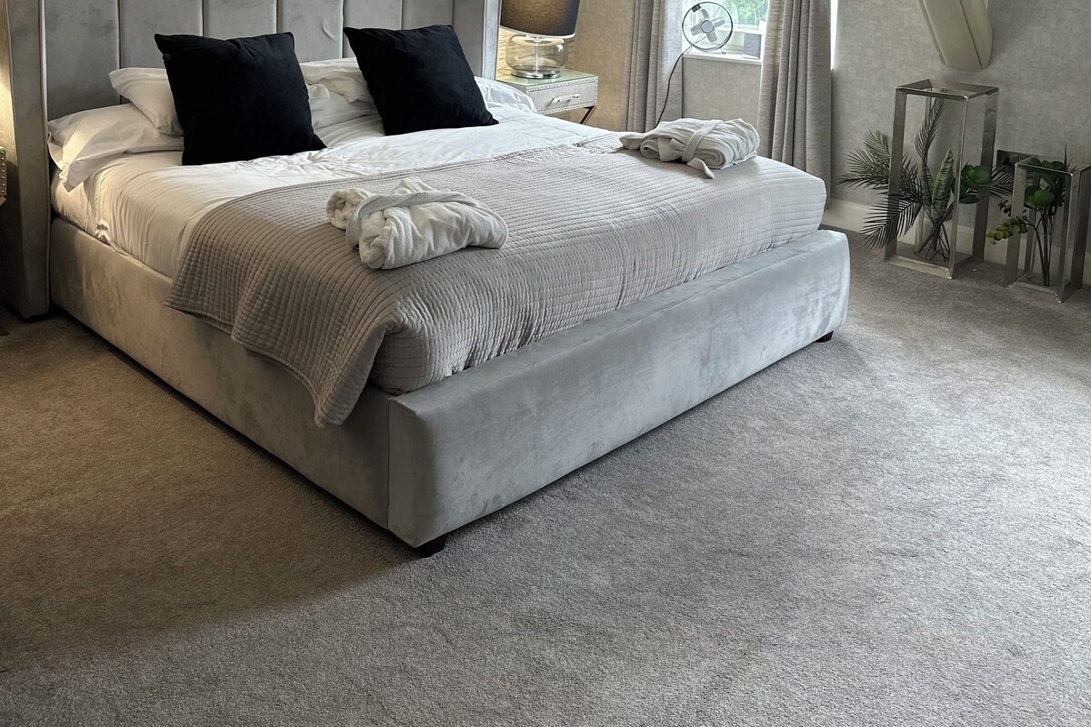 A modern bedroom with a large bed, a nightstand, a lamp, and a fan.