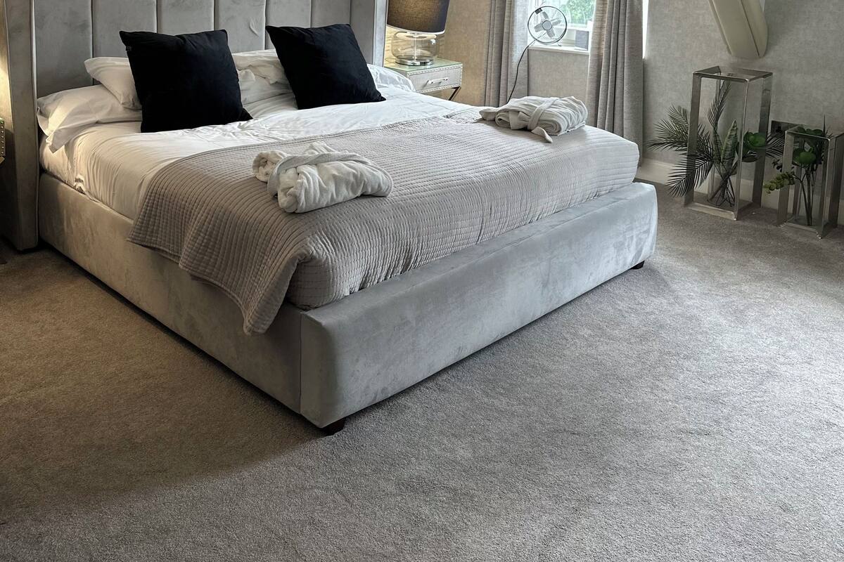A modern bedroom with a large bed, a nightstand, a lamp, and a fan.
