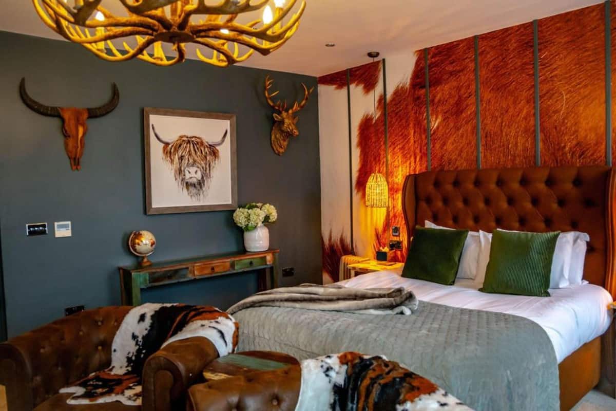A bedroom with a large bed, a tufted headboard, a globe on a nightstand, and wall-mounted antler decorations.