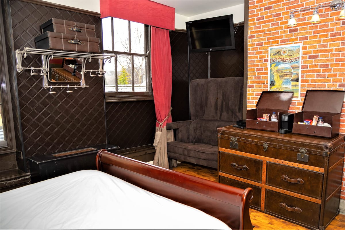 A room with a bed, a dresser with drawers, a television mounted on the wall, and a window with a curtain.