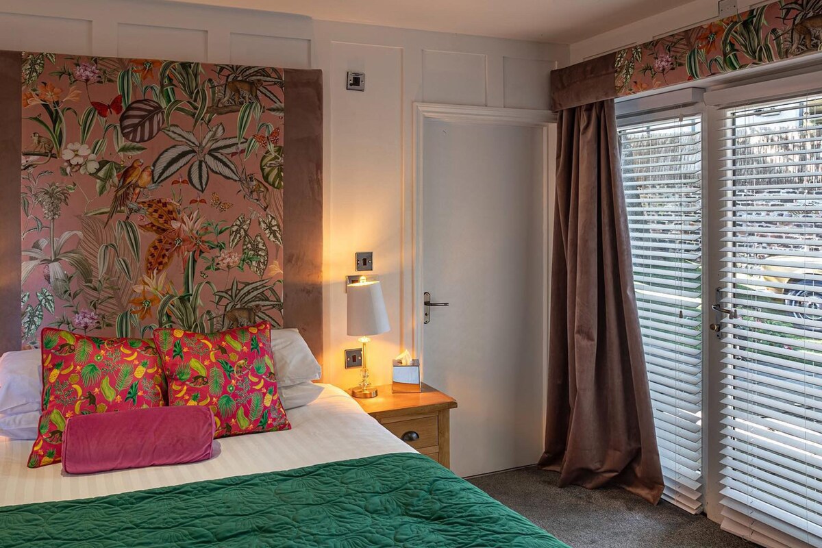 A hotel room with a bed, a nightstand, a lamp, and a window with curtains.