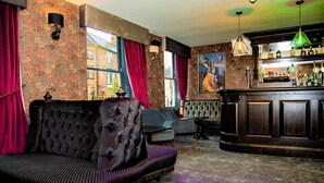 A bar area with a dark wood bar counter and a seating area with a tufted sofa and armchairs. - OYO The Townhouse (Durham)