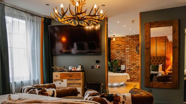 A modern bedroom with a large bed, a television, a fireplace, and a bathroom visible through a glass door. - OYO The Townhouse (Durham)