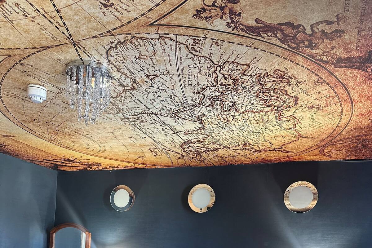 A room with a large bed, two bedside tables with lamps, a wooden dresser, and a ceiling map.
