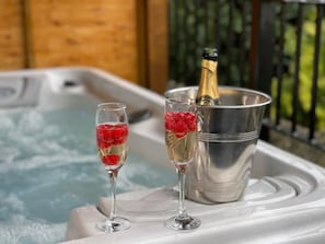 Two champagne flutes with red berries on a tray next to a hot tub.