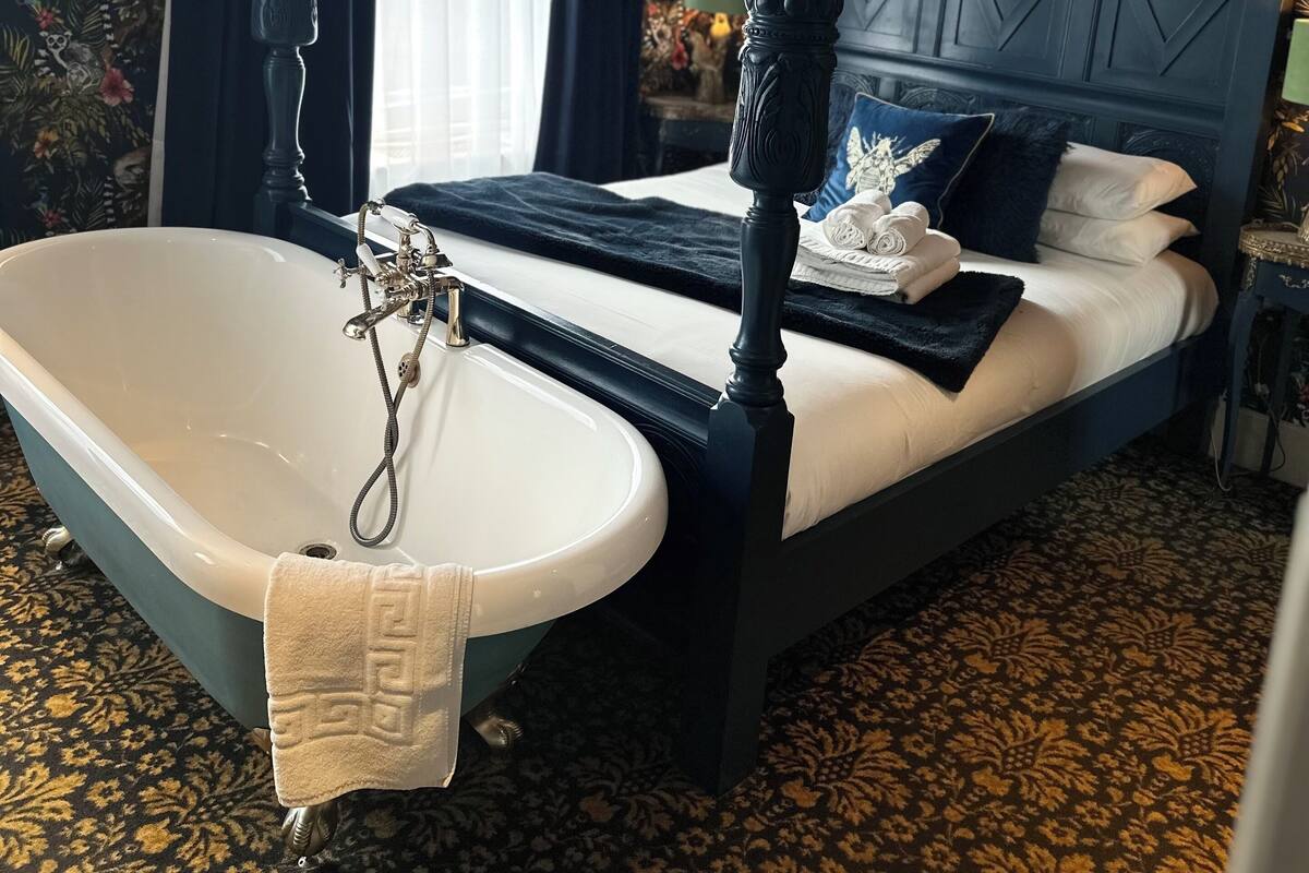 A four-poster bed with a bathtub, a white sink, and a patterned carpet.