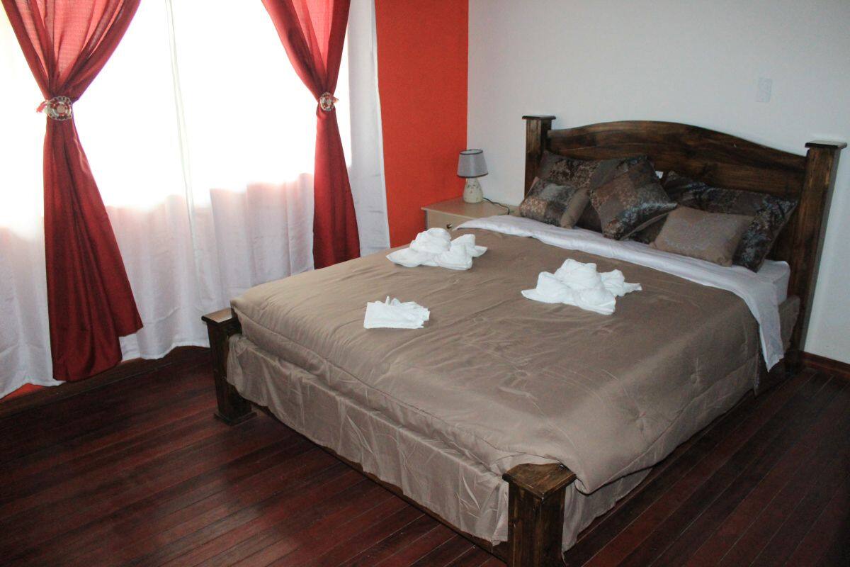 A neatly made bed with a brown bedspread and white towels, a wooden headboard, and a nightstand with a lamp.