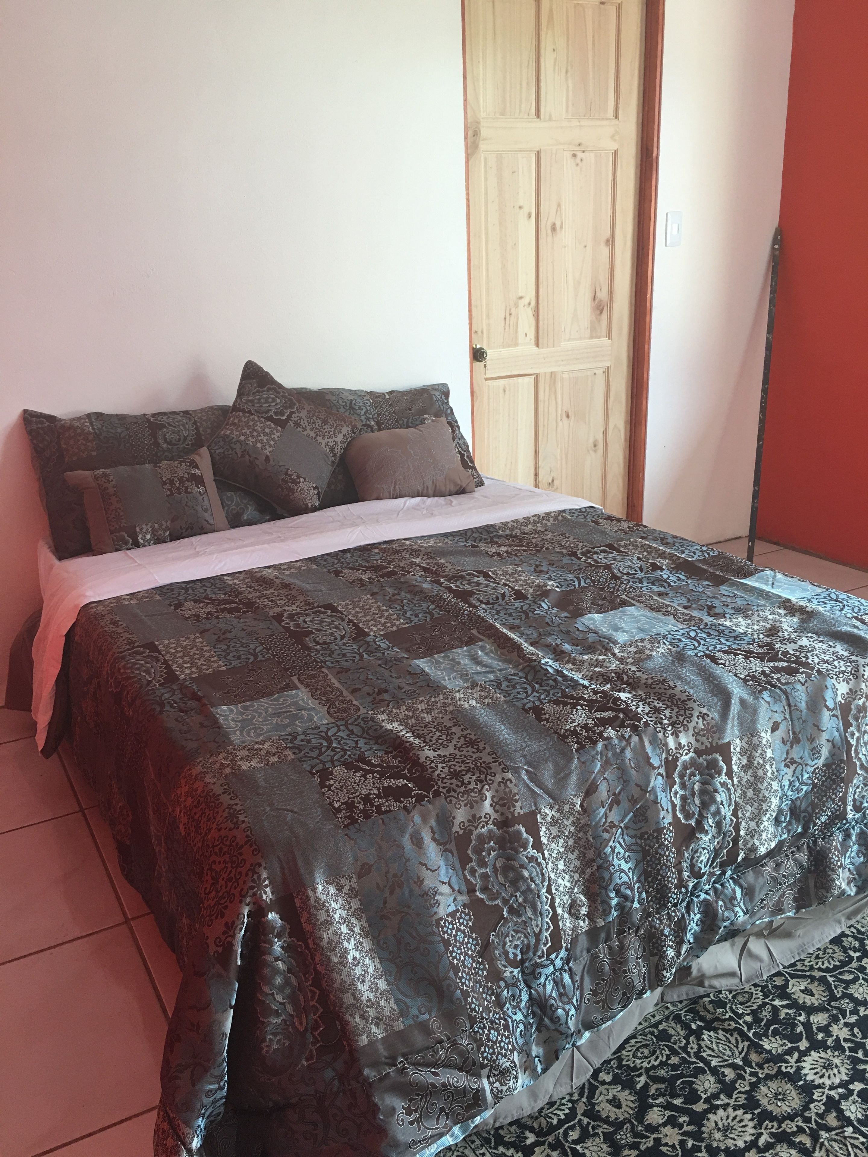 Una cama con un edredón estampado y varias almohadas, una puerta de madera y una pared roja.