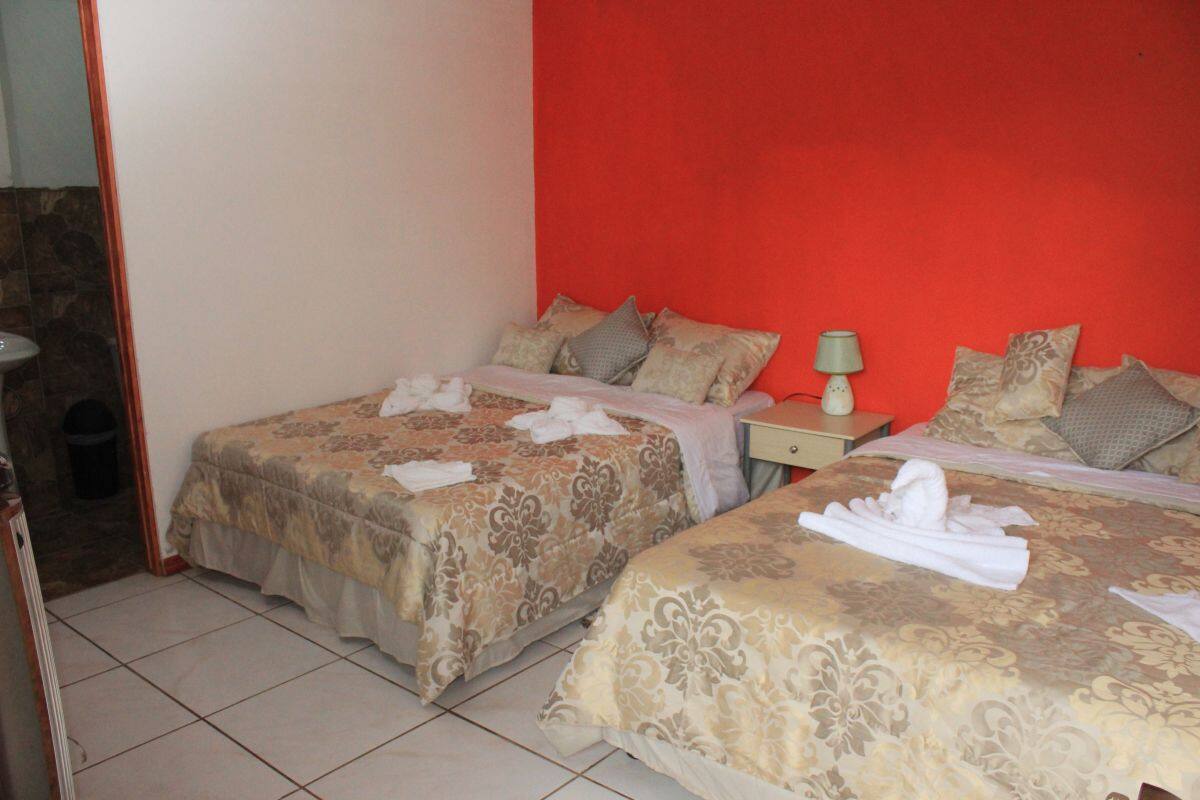 A hotel room with two beds, each with a patterned bedspread and pillows, a bedside table with a lamp, and a red accent wall.