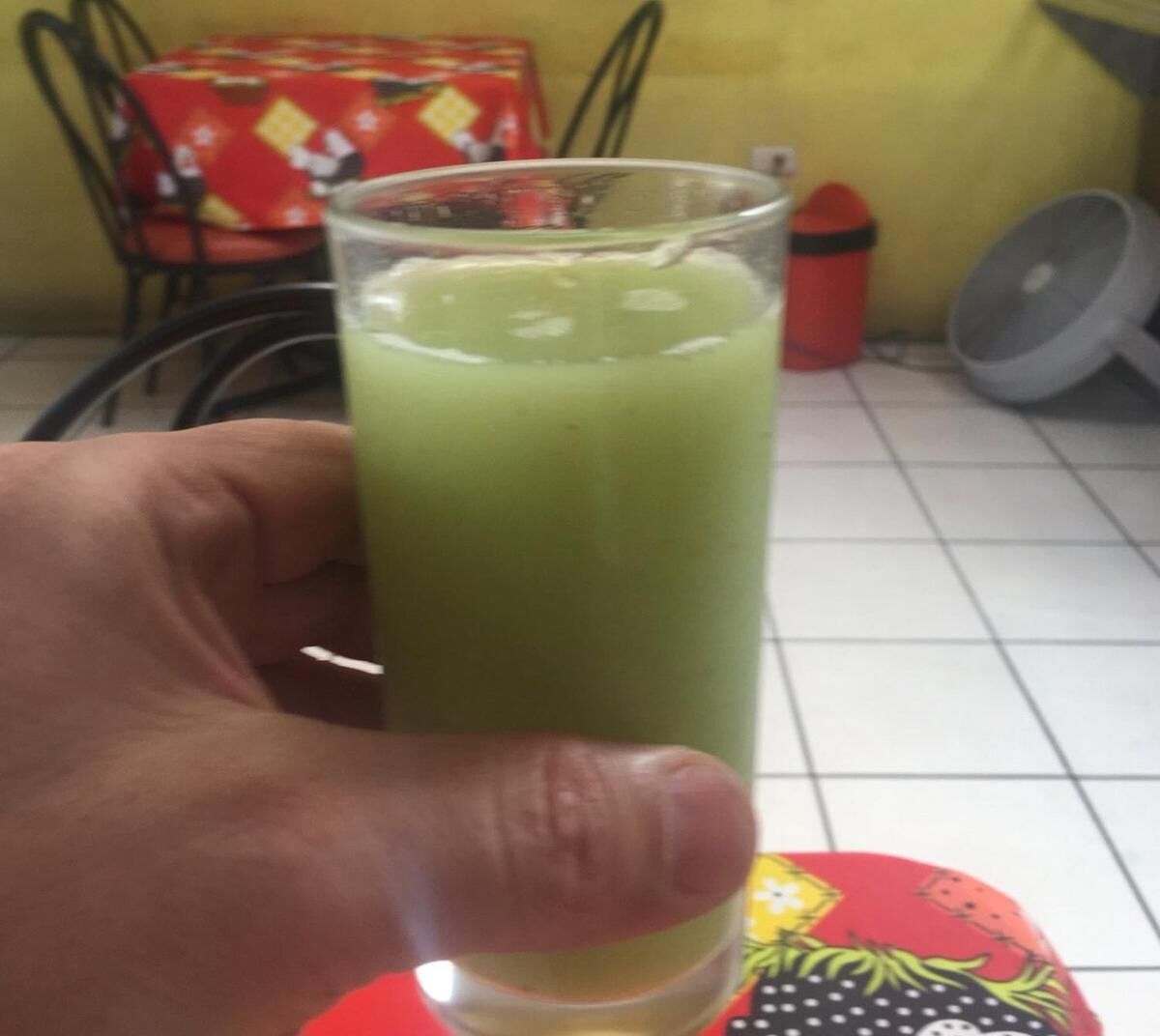 Una mano sostiene un vaso alto con una bebida verde.