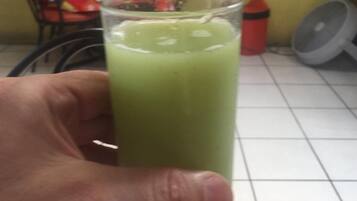 Una mano sostiene un vaso alto con una bebida verde.