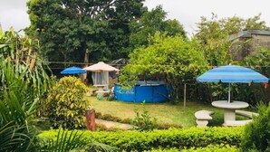 A garden with a blue pool, a table, and a chair under a blue umbrella. - Hotel Your House (Rio Segundo)