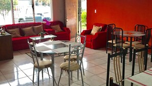 A dining area with red sofas, a glass table, and metal chairs. - Hotel Your House (Rio Segundo)