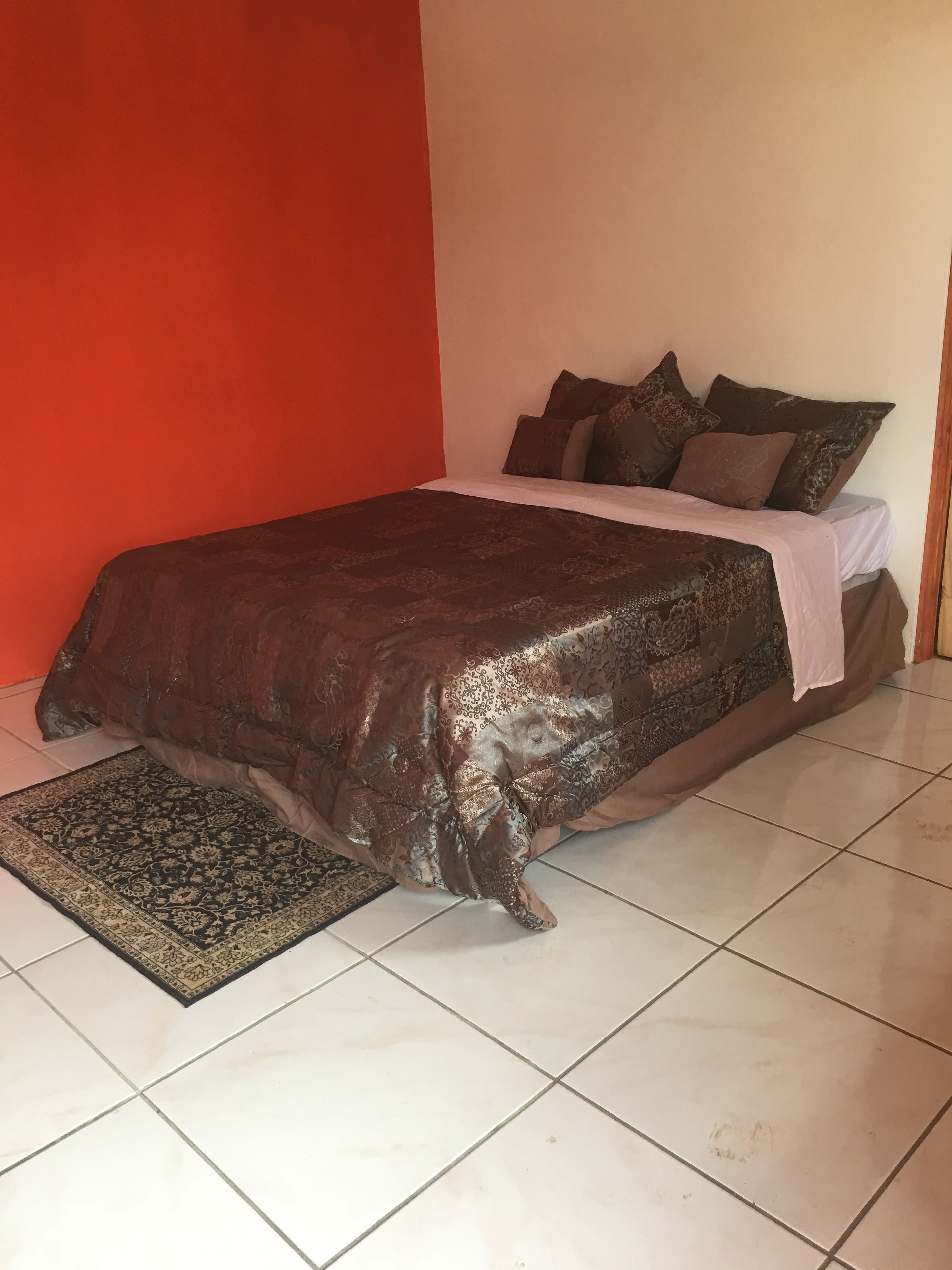 Uma cama com colcha estampada e almofadas, um tapete e piso de azulejos.