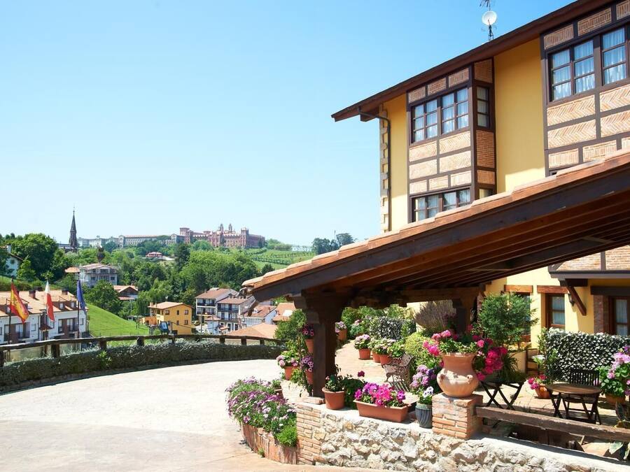 A building with a balcony, potted plants, and a view of a hill with a castle.