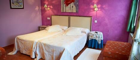 Un dormitorio con una cama doble, dos mesitas de noche, una pequeña mesa redonda con mantel de flores y una silla individual.