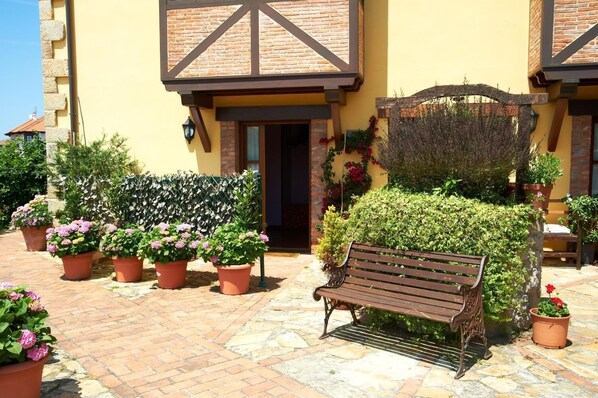 A courtyard with a bench, potted plants, and a building with a yellow facade and dark brown accents.