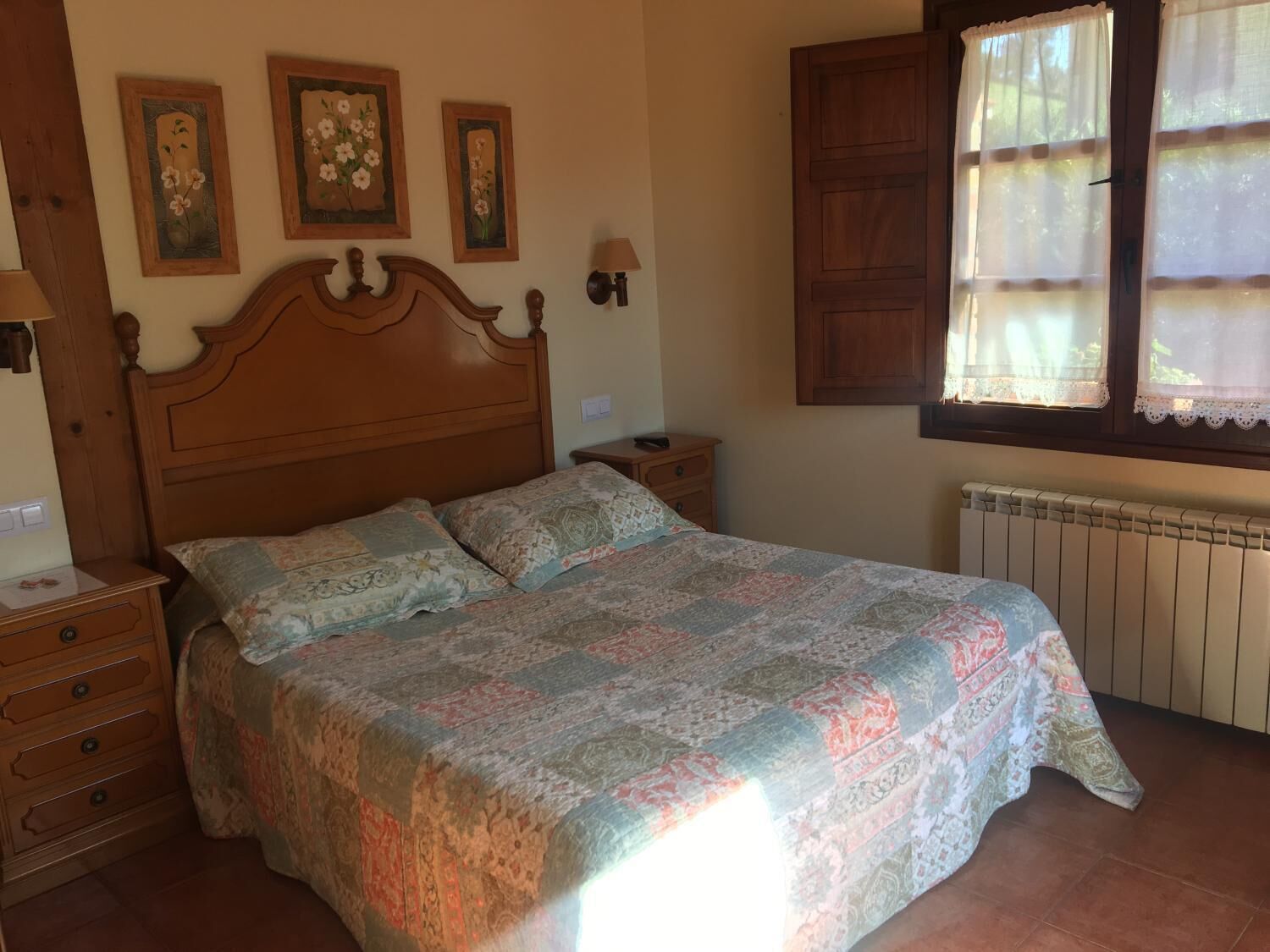 Une chambre à coucher avec un lit en bois, deux tables de chevet, une commode et une fenêtre avec des rideaux.