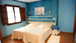 Une chambre à coucher avec un lit double, une table de chevet, une petite table recouverte d’une nappe bleue et un tableau accroché au mur.