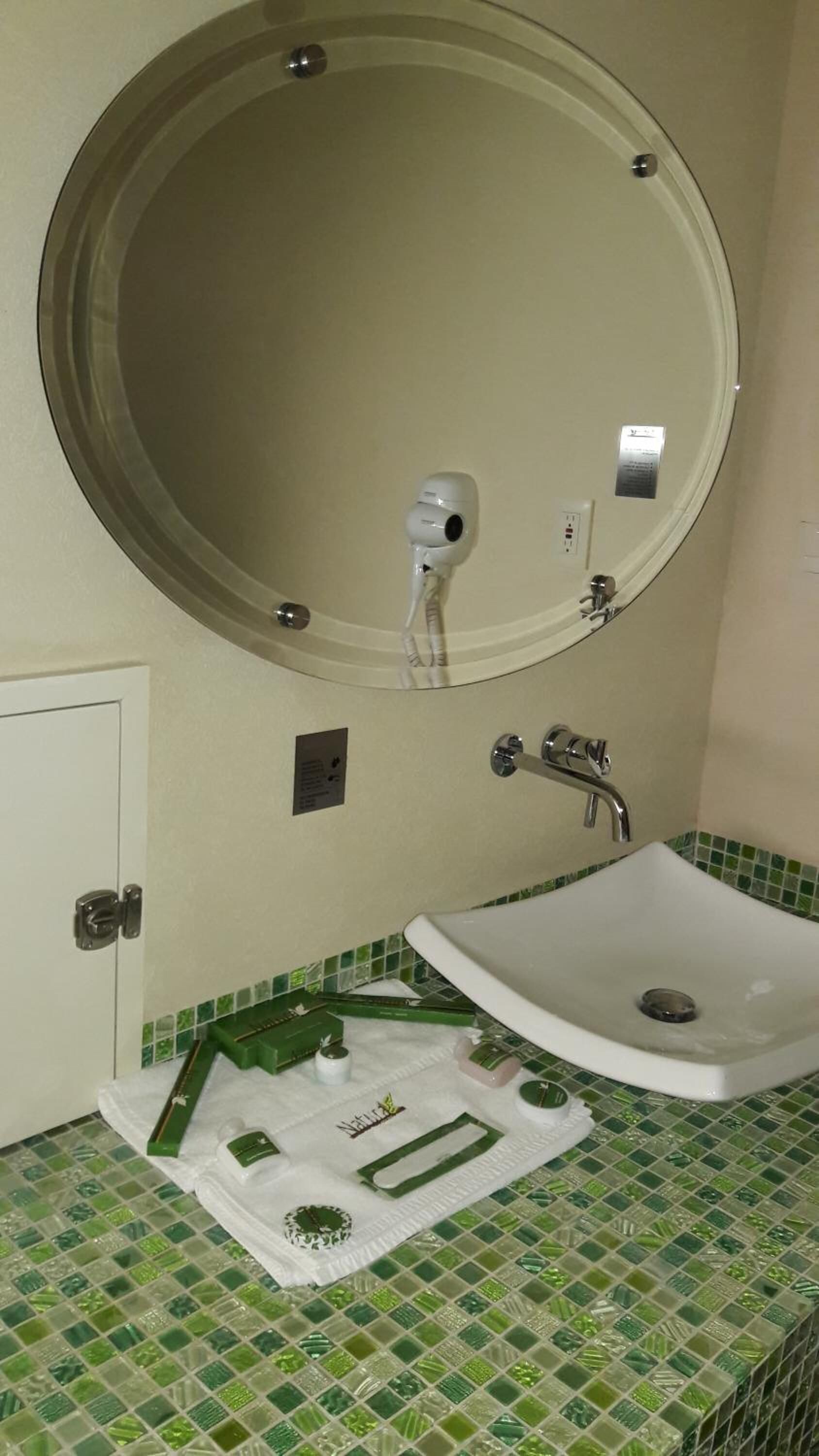 A bathroom with a round mirror, a sink, and green mosaic tiles.