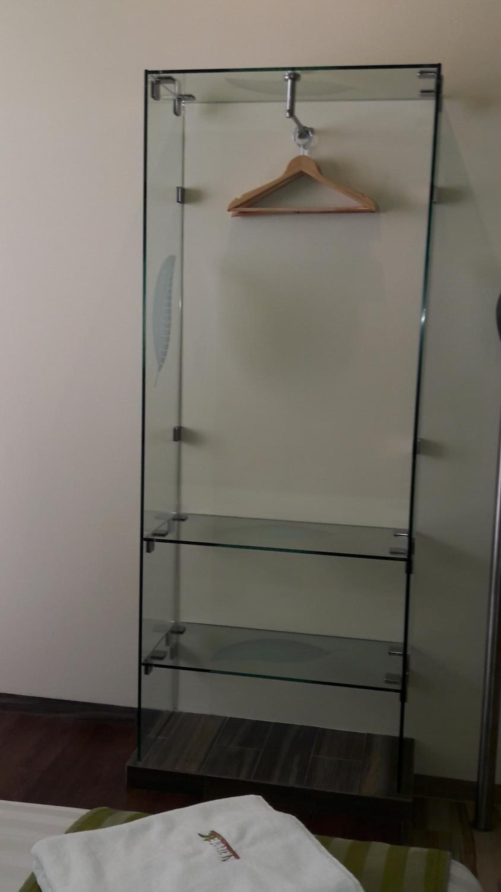 Un meuble étroit et haut, fait d’étagères en verre, comportant trois étagères, un porte-manteau en bois et une petite table recouverte d’une nappe blanche.
