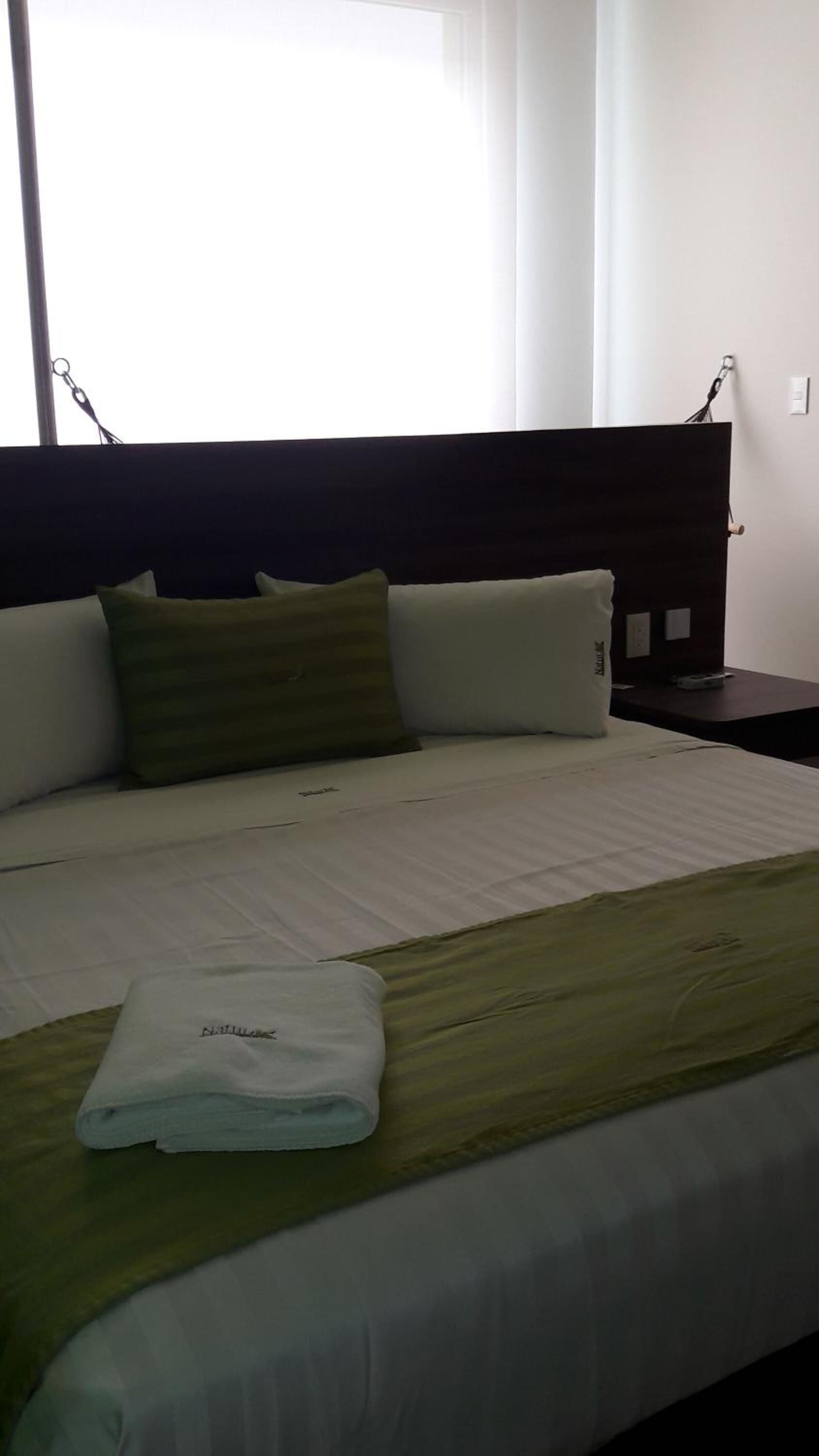 Una cama bien hecha con una manta blanca y verde a rayas, una toalla blanca doblada y dos almohadas.
