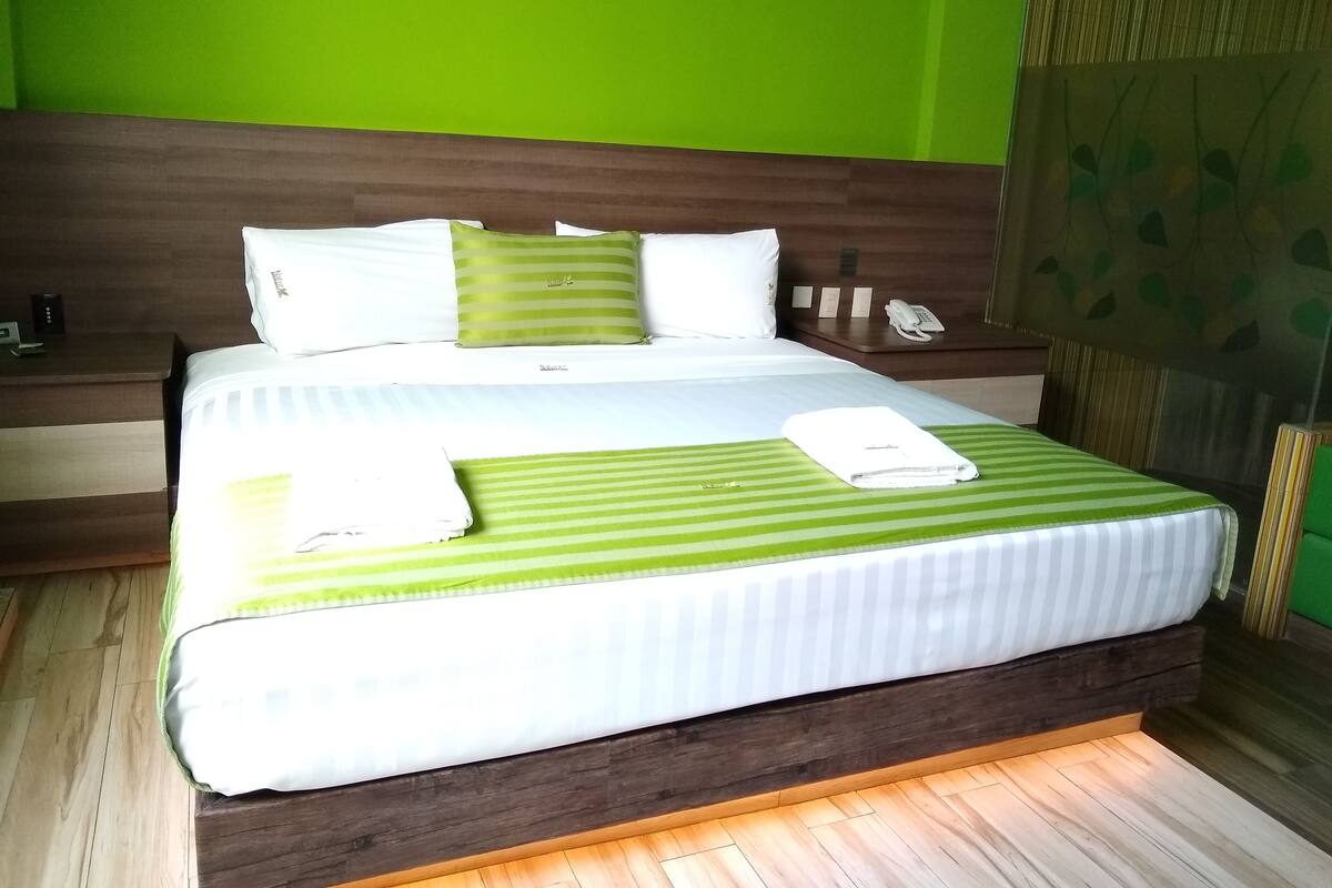 Un lit bien fait, avec une literie à rayures vertes, un oreiller blanc et une serviette pliée posée sur le lit.