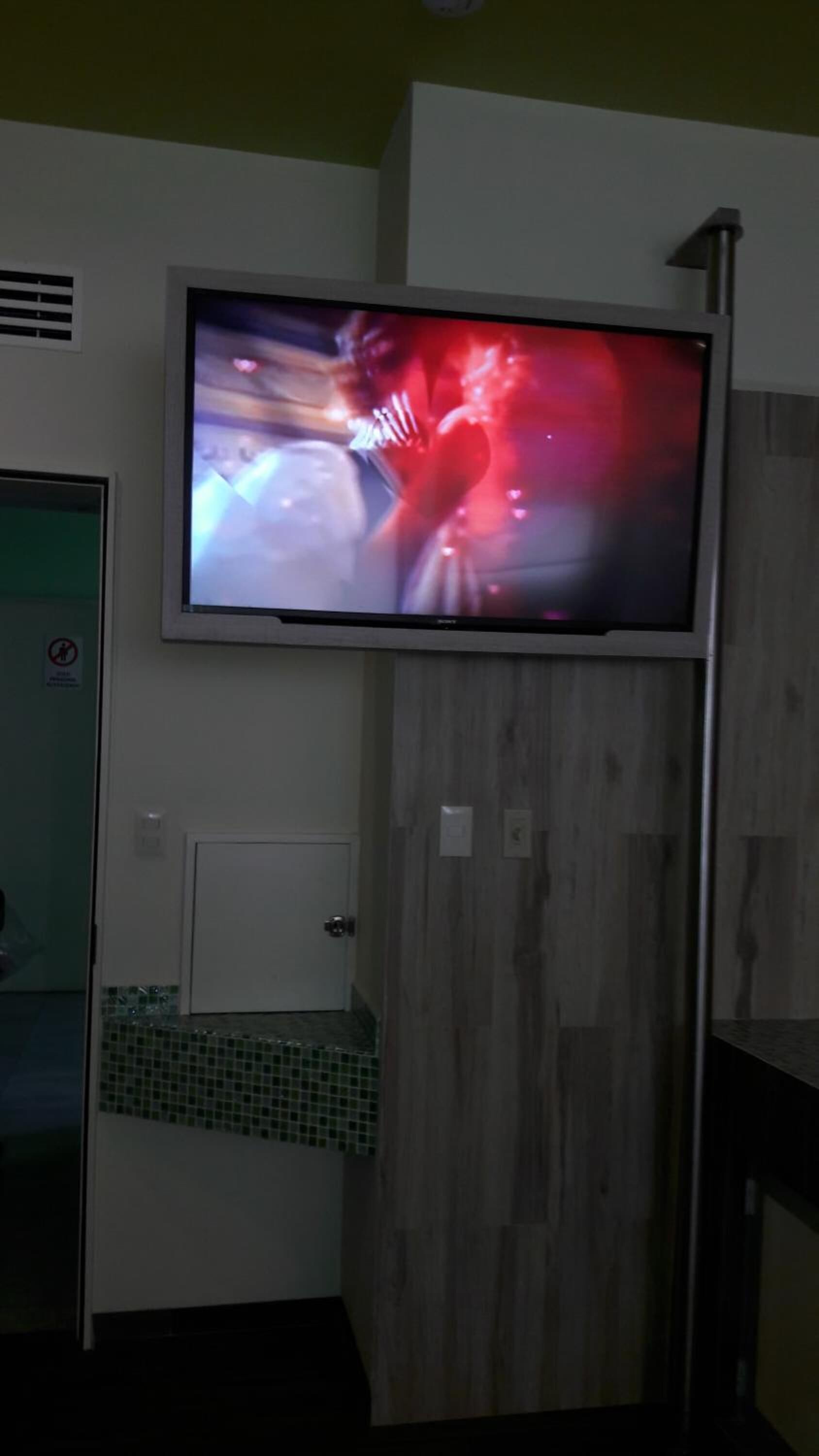A television mounted on a wall in a room with a wooden panel and a door with a glass panel.