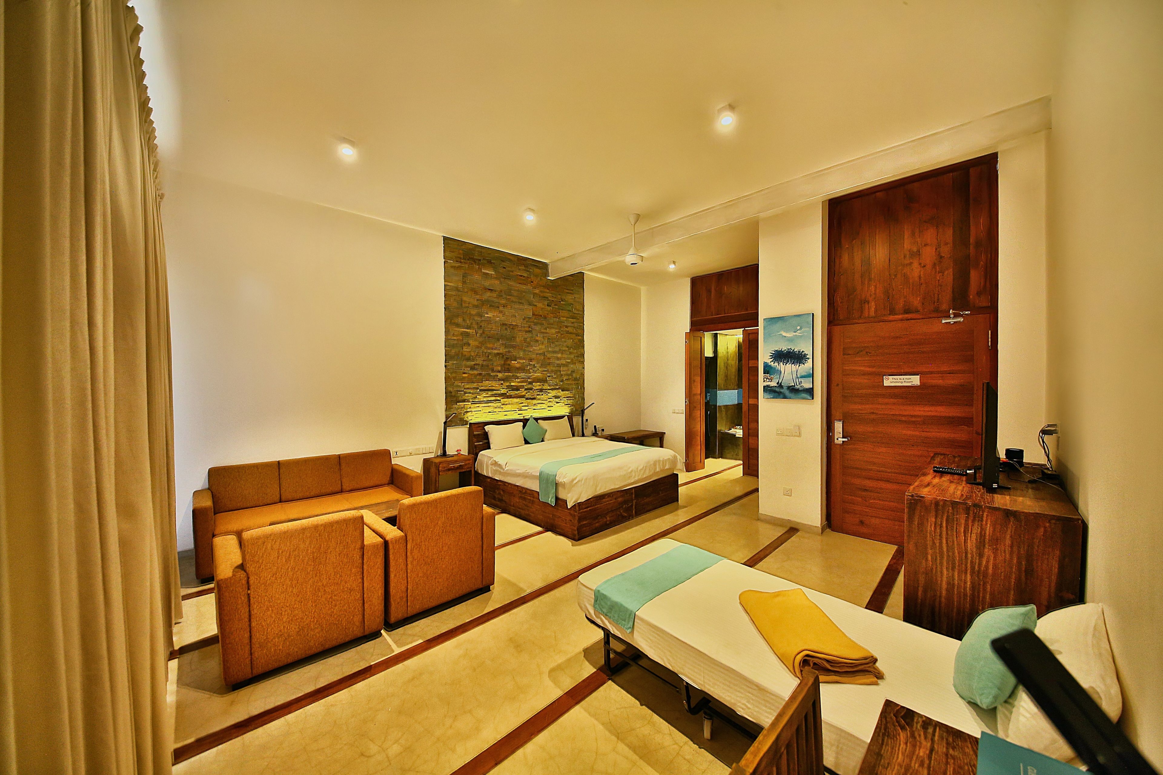 A hotel room with a sofa, two single beds, a wooden wardrobe, and a stone wall.