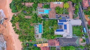 Vista aérea de un complejo turístico con piscina, varias edificaciones y una playa.