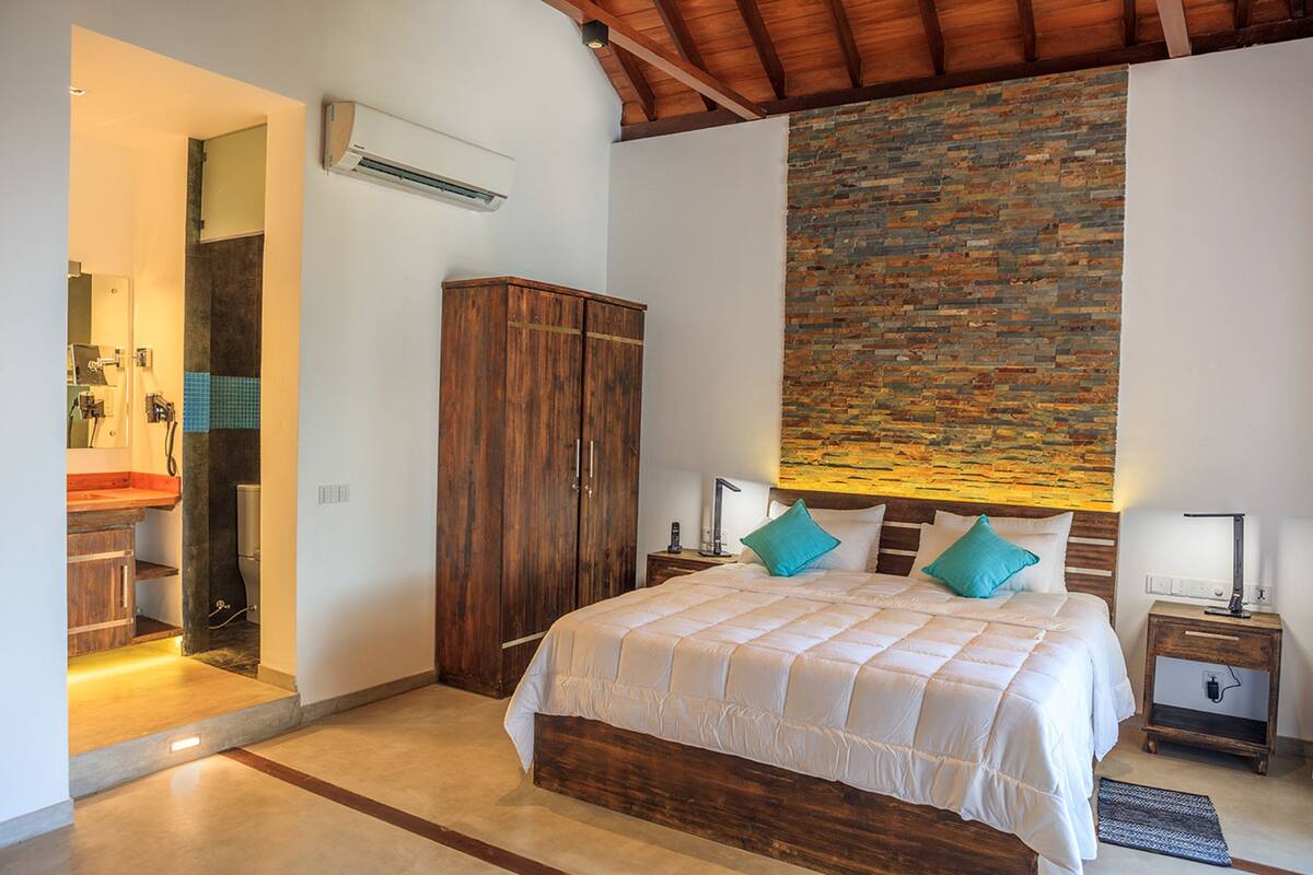 Une chambre avec un lit en bois, un mur d’accent en pierre, une armoire en bois et une salle de bain avec un lavabo et un miroir.