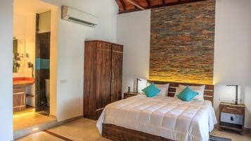 A bedroom with a wooden bed, a stone accent wall, a wooden wardrobe, and a bathroom with a sink and mirror.