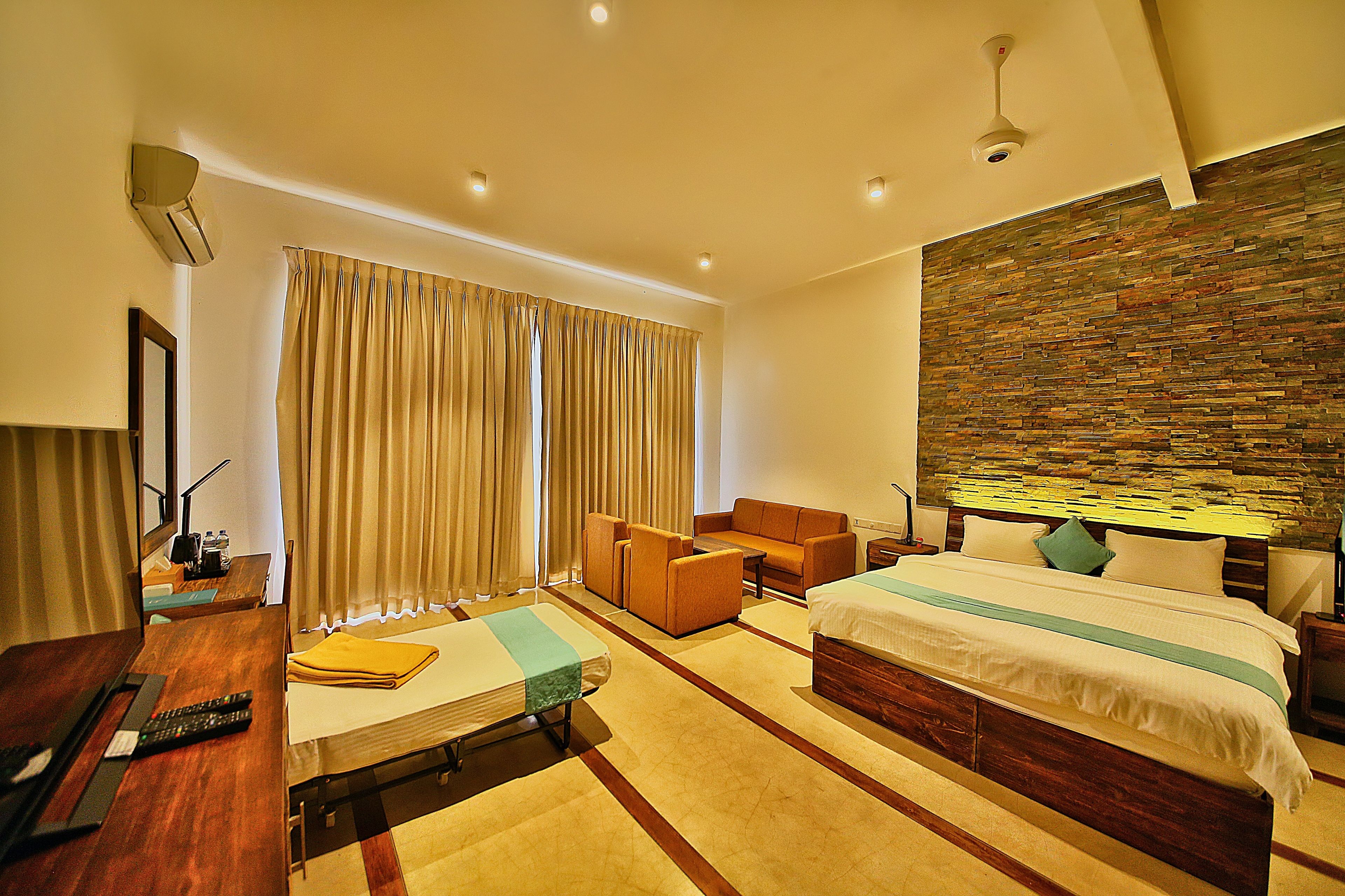 A hotel room with a bed, a desk, a chair, a small table, and a stone wall.