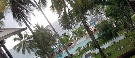 A view of a pool area with palm trees and a beach in the background.