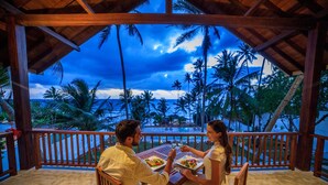 Una pareja cenando en una mesa de madera con vista al océano y palmeras.