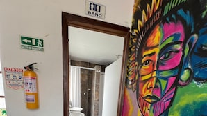 Baño con ducha, inodoro y lavamanos. Hay un extintor y una barandilla en la pared.