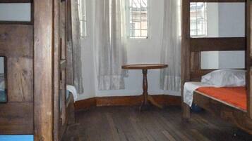 A room with wooden bunk beds, a small table, and a window with curtains.