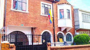 Una casa de ladrillo de dos pisos con cerca de metal negro, una bandera y un pequeño jardín.