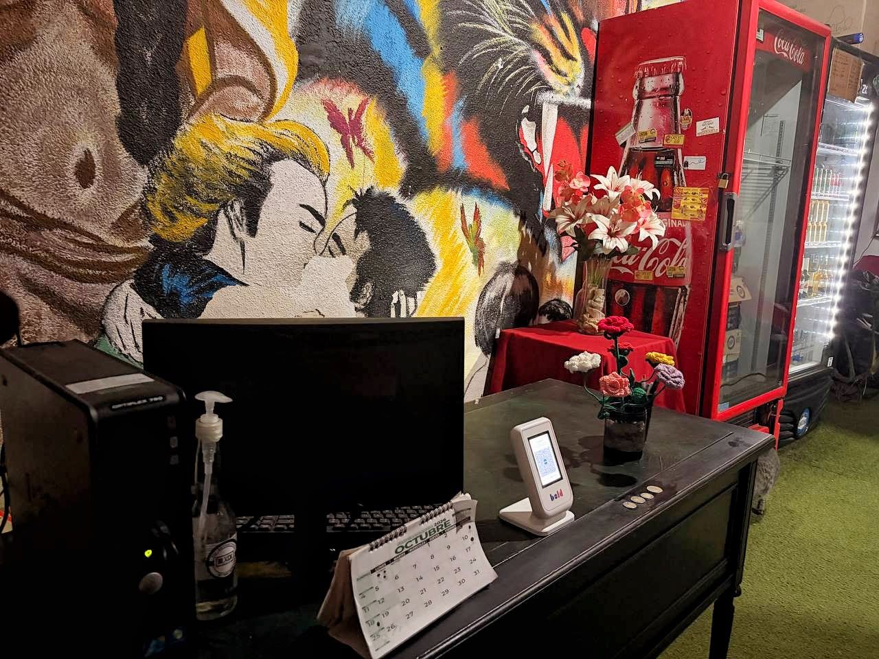 Una mesa de recepción con un calendario, un teléfono, un dispensador de gel antibacterial y un refrigerador de Coca-Cola.