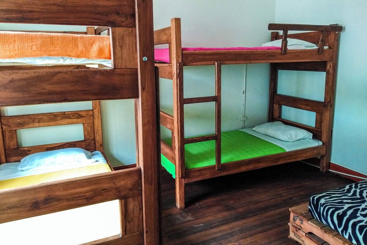 Een slaapkamer met stapelbedden, houten frames en groen beddengoed.