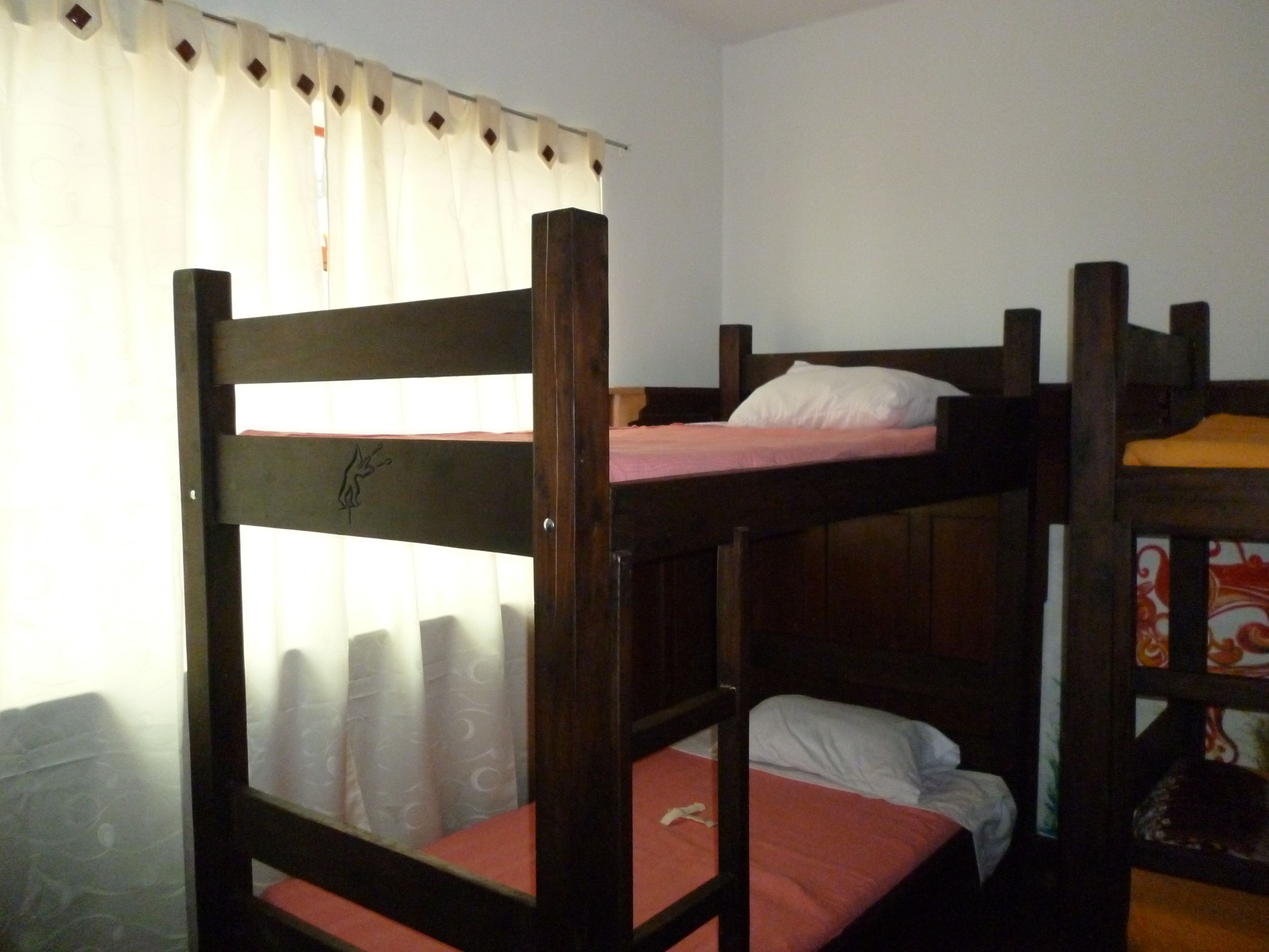 A bunk bed room with a curtain partially drawn, a wooden headboard, and a bed with a white pillow.