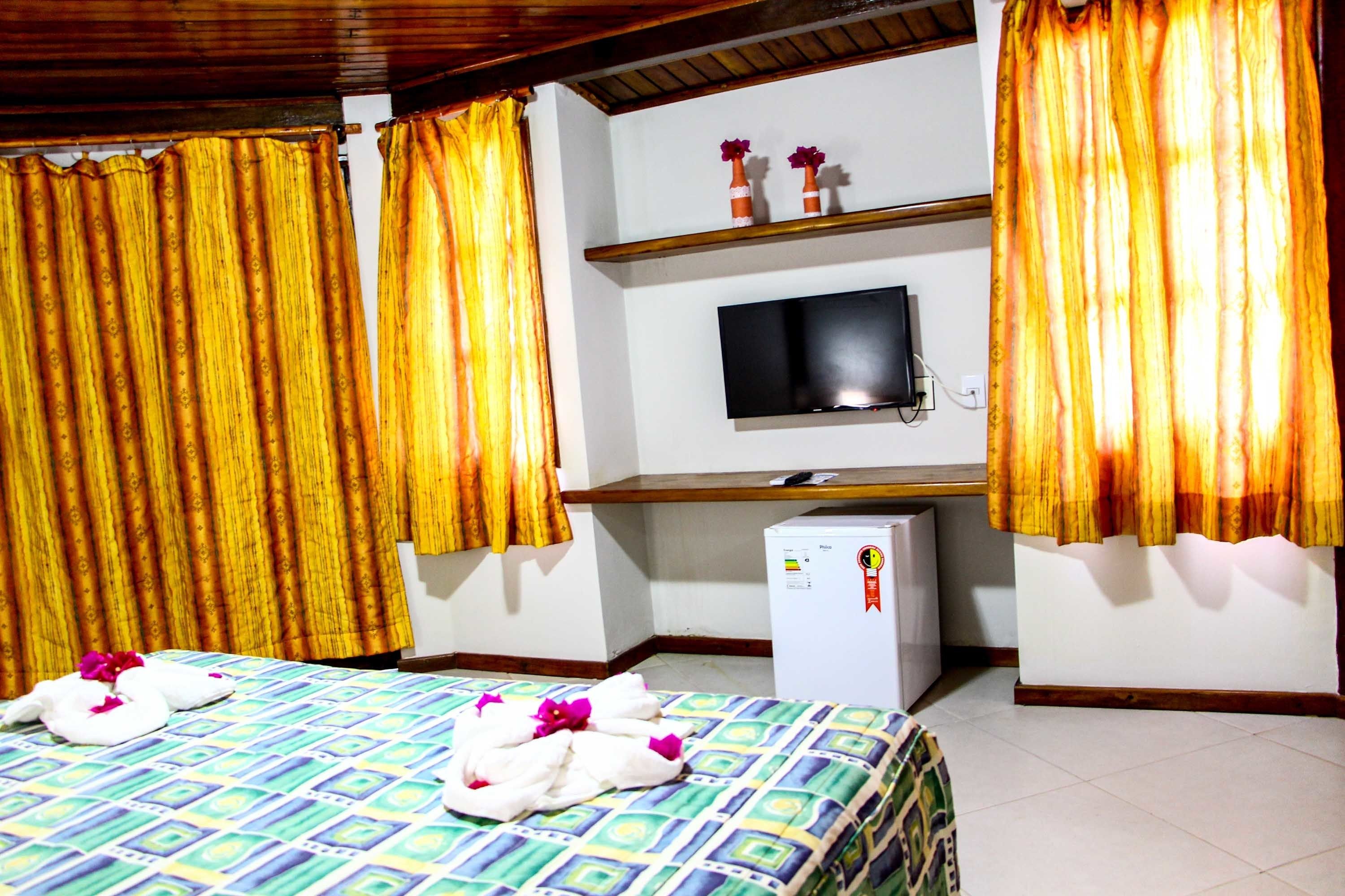 Habitación de hotel con dos camas, televisión, un refrigerador pequeño y cortinas amarillas.