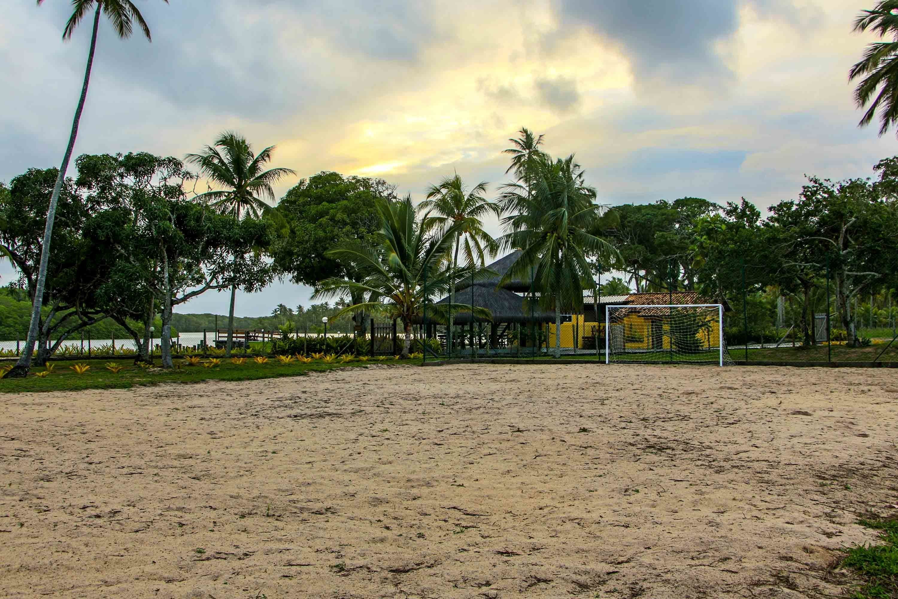 A sandy beach with a soccer goal, palm trees, and a thatched-roof structure.