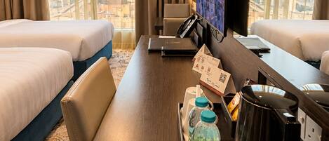 A hotel room with two beds, a desk with a laptop, a television, and a cityscape view.