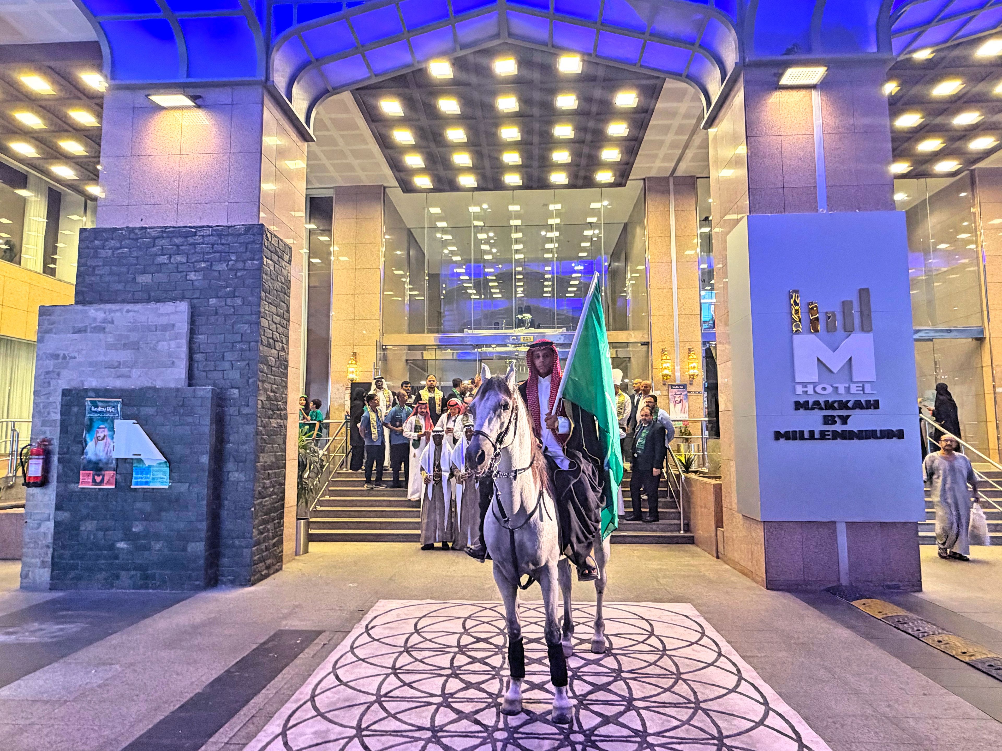 A hotel entrance with a large sign, a horse with a flag, and a crowd of people.