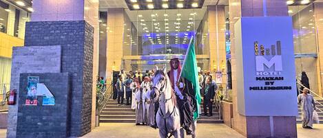 A hotel entrance with a large sign, a horse with a flag, and a crowd of people.