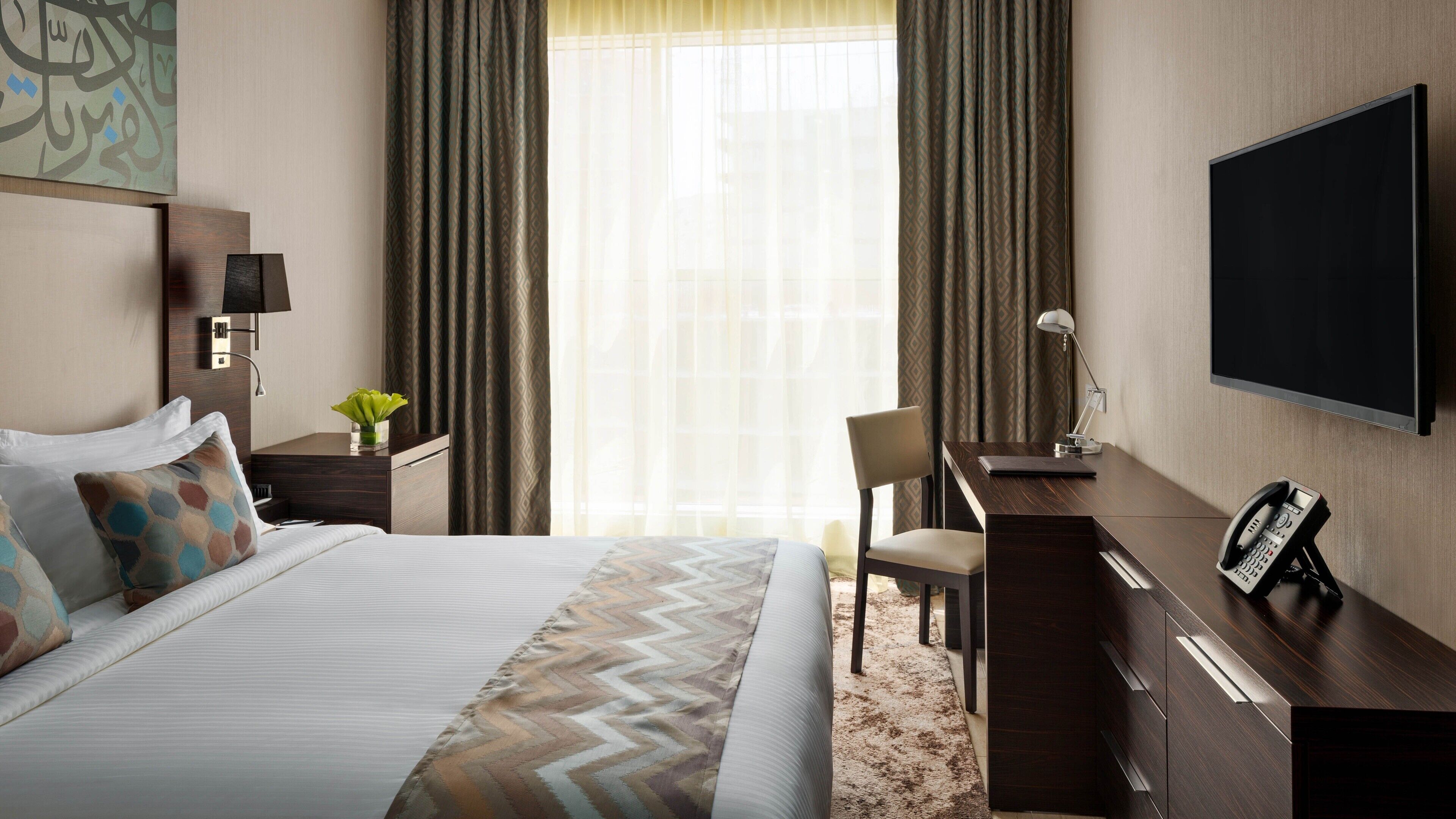 Une chambre d’hôtel équipée d  ’un lit, d’un bureau, d’une chaise, d’une télévision et d’un téléphone.
