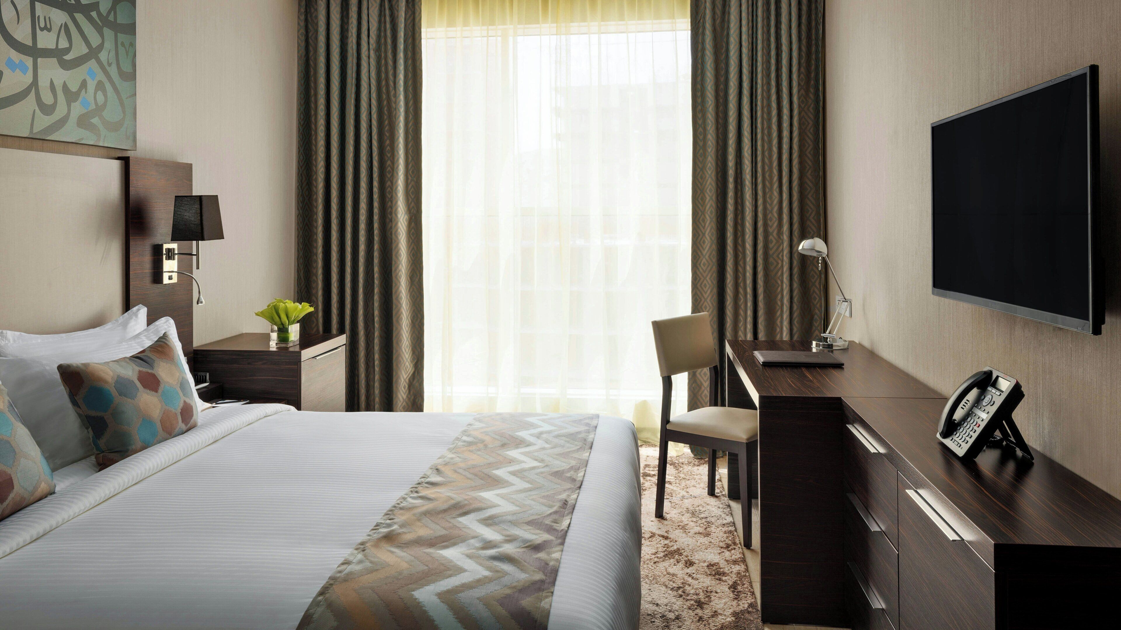 Une chambre d’hôtel équipée d’un lit, d’un bureau, d’une chaise, d’une télévision et d’un téléphone.